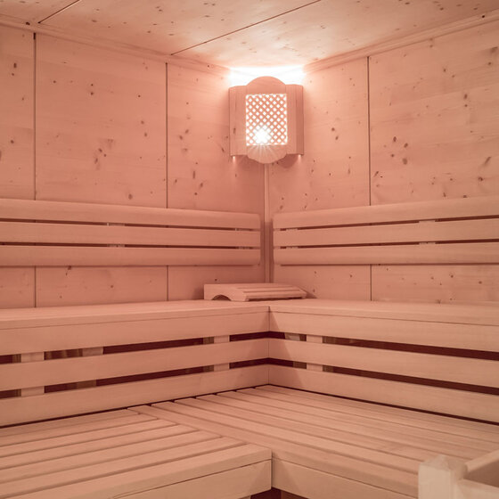 Eine moderne Holzsauna mit hellen, L-förmig angeordneten Bänken, warmer Beleuchtung.
