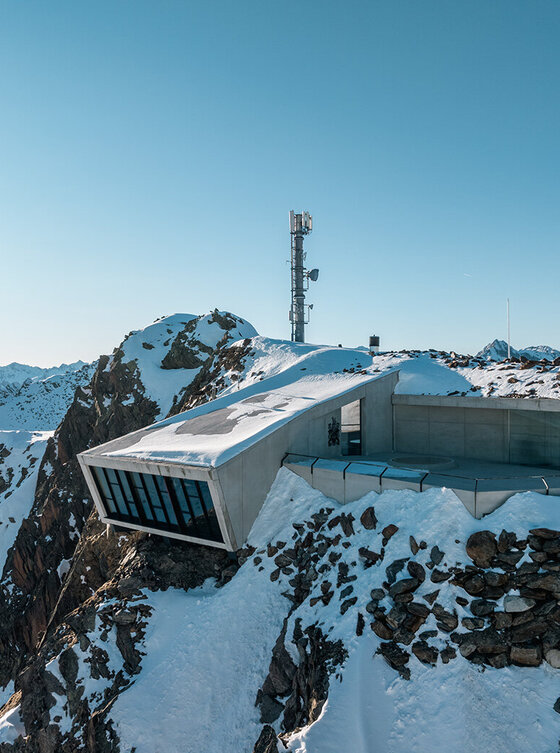 Ein modernes Gebäude aus Glas und Beton auf einem schneebedeckten Berggipfel unter einem strahlend blauen Himmel. Es handelt sich um das 007 Elements Museum mit Panoramablick und Hightechexponaten zu den James-Bond-Filmen.
