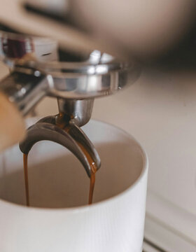 Nahaufnahme einer Espressomaschine, die frischen Espresso in eine weiße Keramiktasse einschenkt, wobei aus dem Siebträgerauslauf satte braune Kaffeeströme fließen.