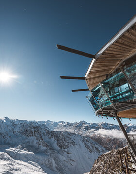 Ein modernes Glasgebäude mit Blick auf schneebedeckte Berggipfel unter einem strahlend blauen Himmel und strahlendem Sonnenschein.