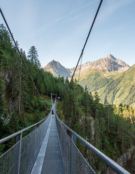 Eine lange Hängebrücke über ein bewaldetes Tal mit Bergen im Hintergrund unter einem klaren Himmel.