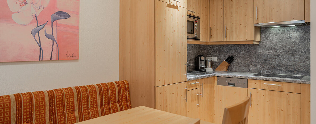 Eine gemütliche Küche mit hellen Holzschränken und einem passenden Esstisch mit zwei Stühlen und einer gepolsterten Bank. Es gibt eine Blume Malerei an der Wand und grauem Marmor Backsplash hinter dem Herd und Zähler Geräte.