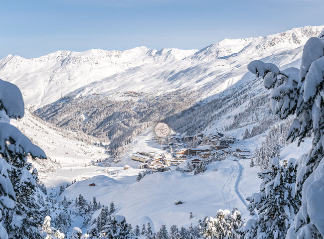 Ein verschneites Alpendorf liegt in einem Tal, umgeben von Bergen, Kiefern und frisch verschneiten Hängen unter einem strahlend blauen Himmel. Winterliches Lagenbild von Gurgl mit dem Alpenresidenz Logo in der Mitte des Bildes.
