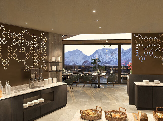 Ein moderner Essbereich mit dekorativen Wandpaneelen, Buffet-Theken und Körben auf dem Tresen. Große Fenster geben den Blick frei auf eine Terrasse mit Tischen und Stühlen und die schneebedeckten Berge im Hintergrund.