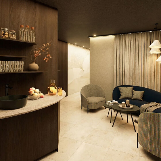 Eine gemütliche, moderne Lounge mit einem geschwungenen Sofa, zwei Sesseln, kleinen runden Tischen und sanfter Beleuchtung. In den Regalen stehen Gläser und Flaschen über einer Theke mit Obst und Glaswaren. Beigefarbene Vorhänge bedecken eine Wand.