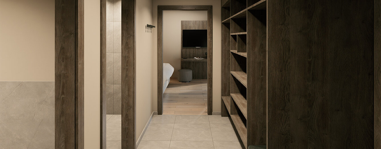 Ein schmaler Flur mit hellen Böden und Wänden, mit dunklen Holztürrahmen und Regalen auf der rechten Seite; am Ende des Flurs ist ein Raum zu sehen.