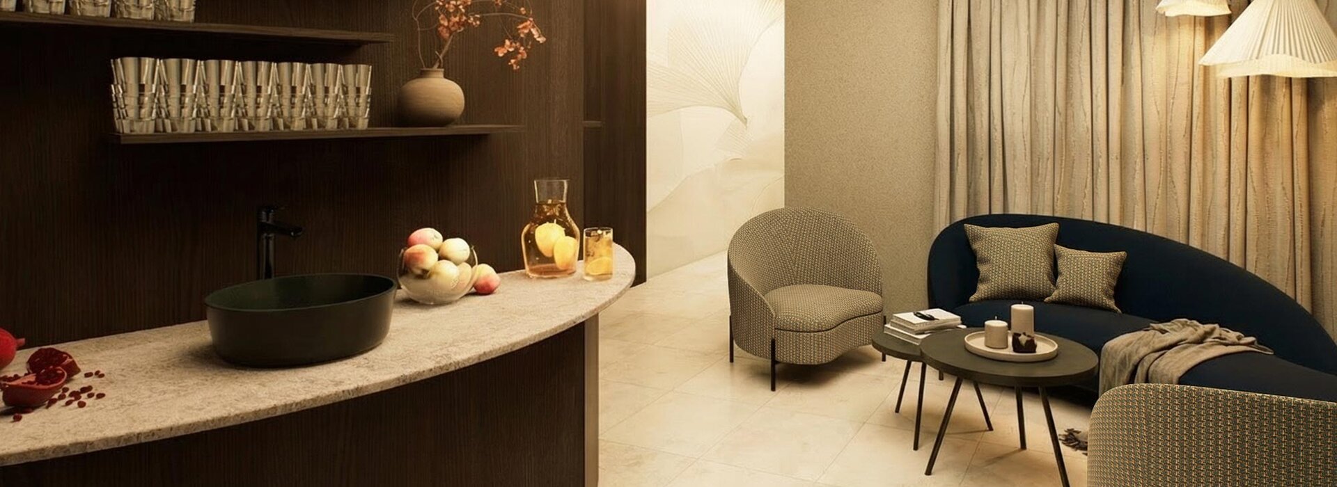 Moderner, warm beleuchteter Loungebereich mit einem geschwungenen Sofa, zwei Sesseln und Couchtischen. Ein Tresen bietet Platz für Gläser, Obst und Glaswaren. Neutrale Töne und sanfte Beleuchtung schaffen ein gemütliches, elegantes Ambiente.